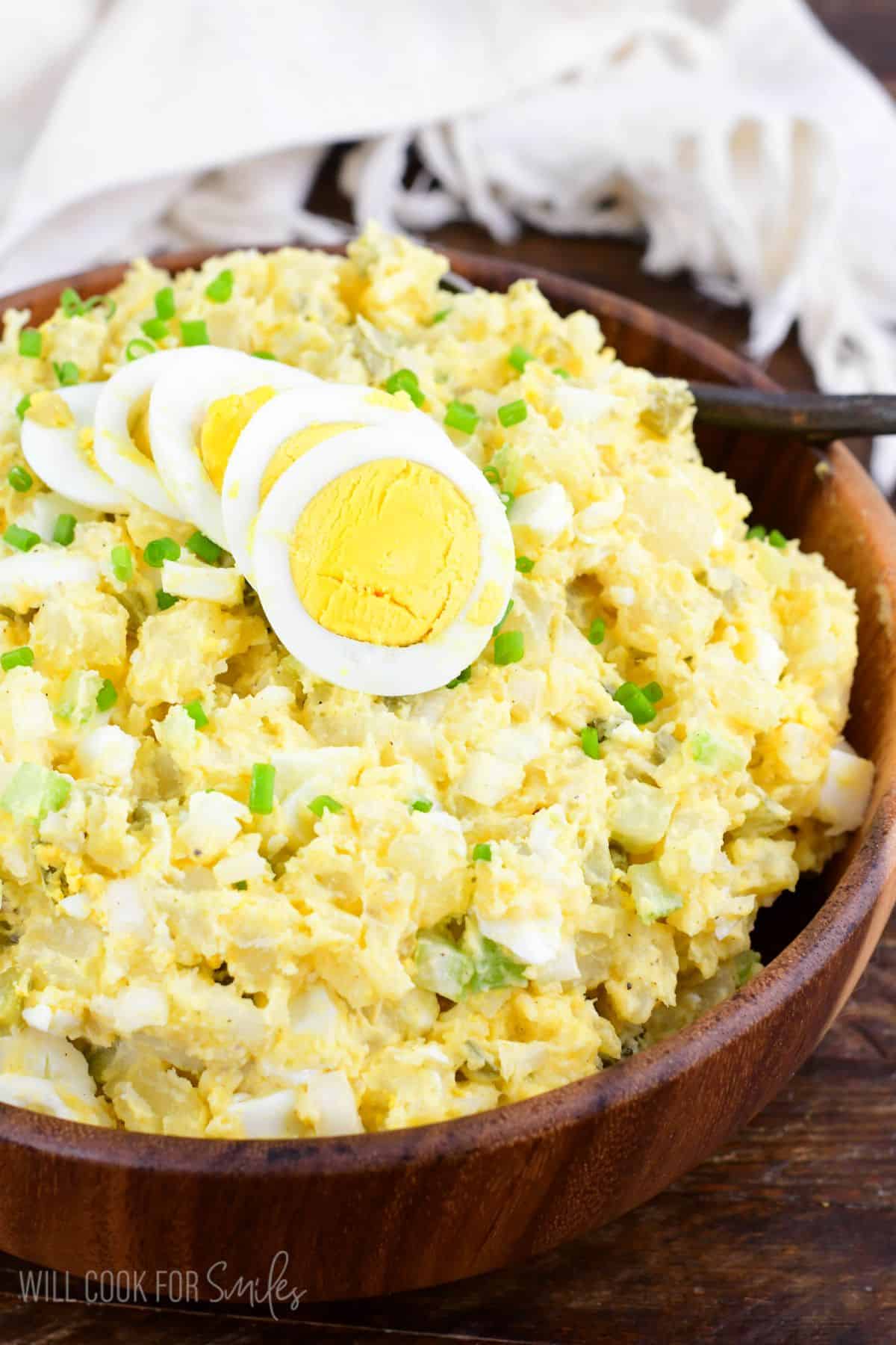 a wooden bowl filled with mustard and pickles potato salad.