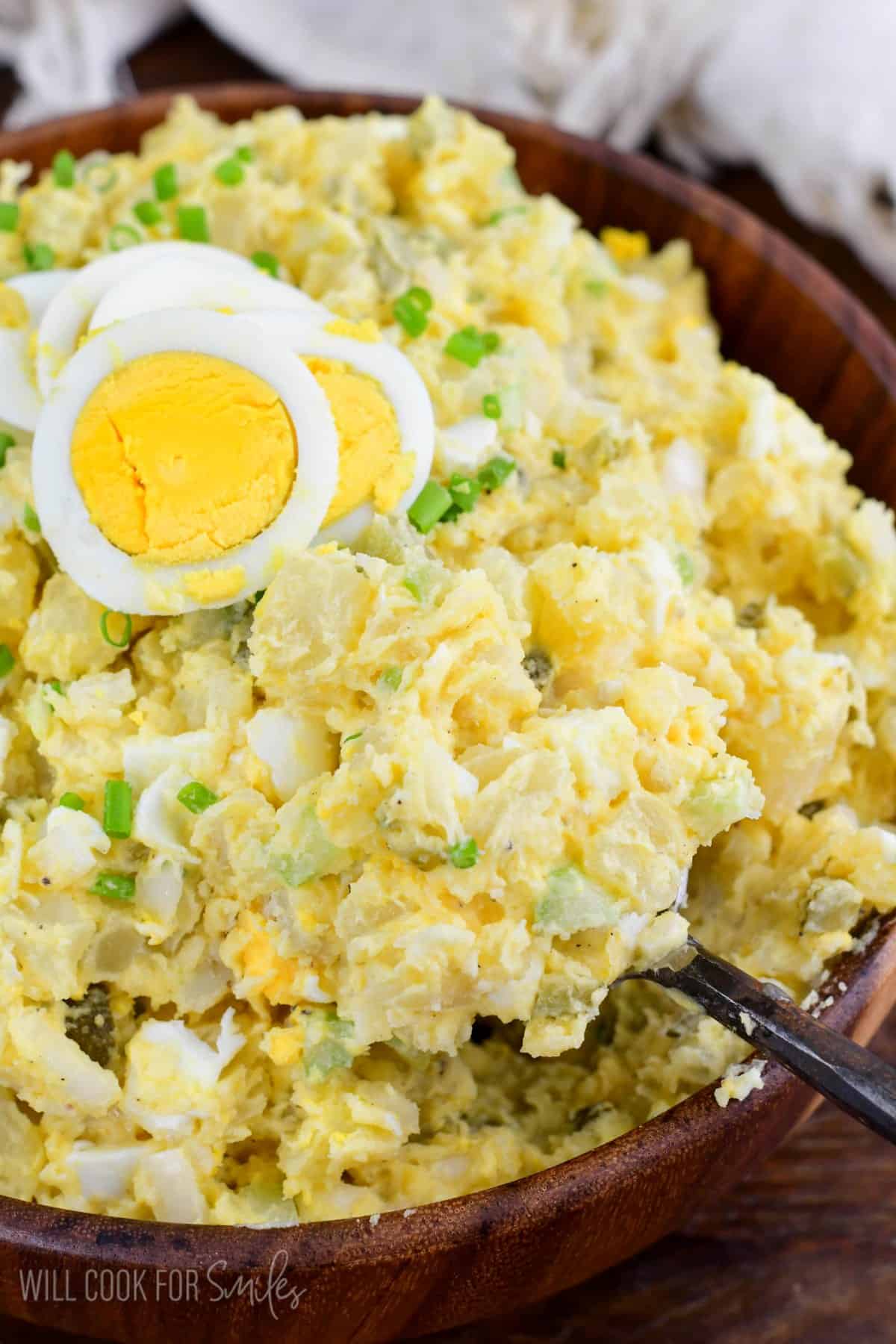 scooping out some southern potato salad from the bowl and sliced egg on top.