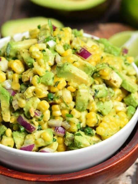 Avocado Corn Salad in a bowl with avocado sliced in half in the background.