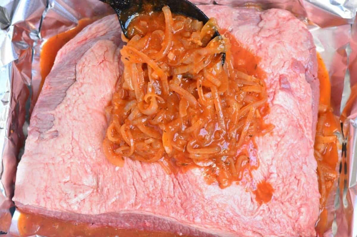 pouring French onion sauce over the uncooked brisket in the foil in the roasting pan.