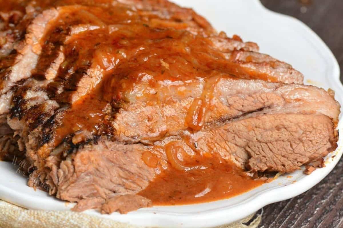 sliced point side of the French onion brisket covered in sauce on the plate.