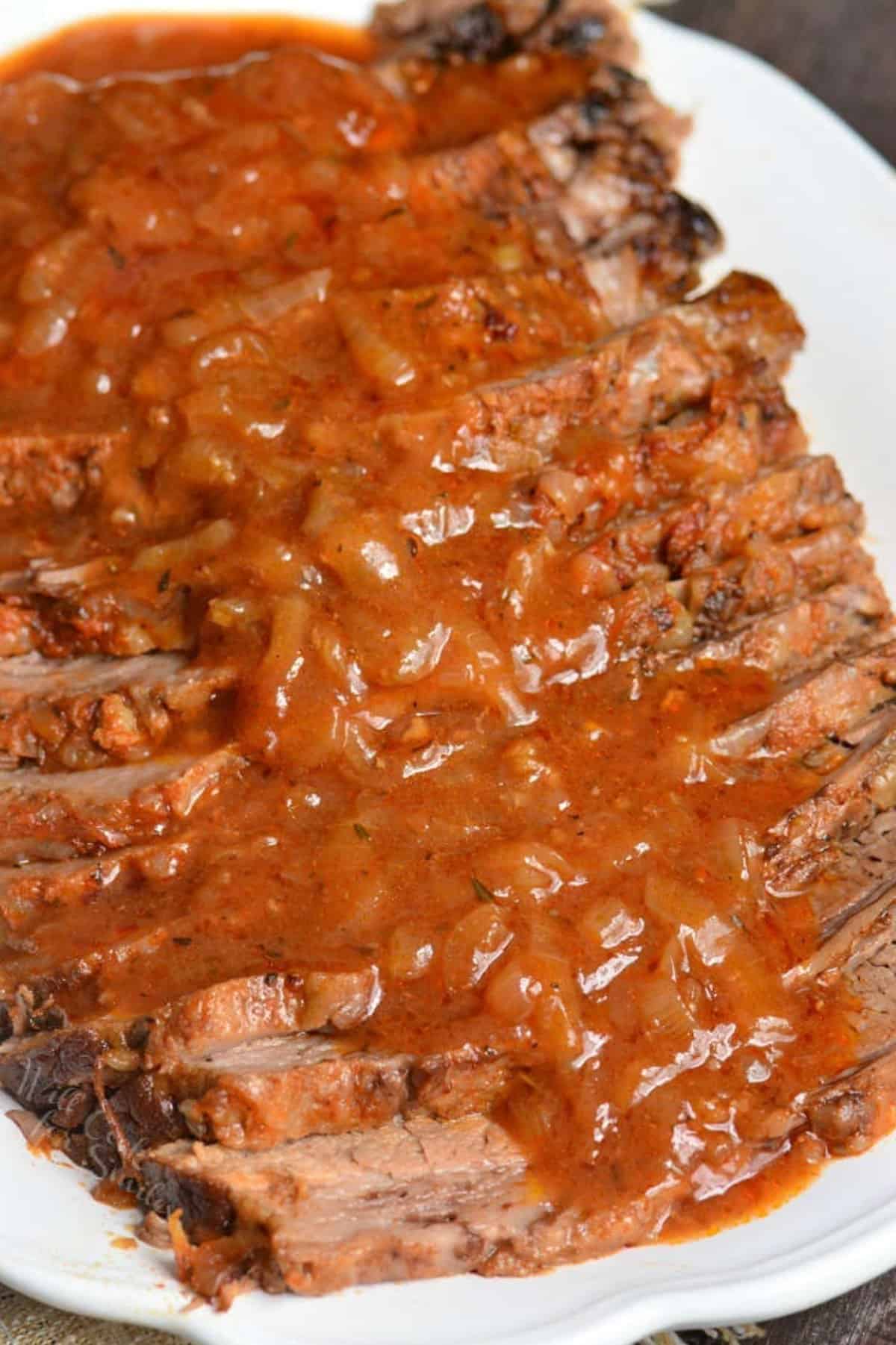 juicy and tender fall apart beef brisket sliced and topped with French onion sauce on a white plate.