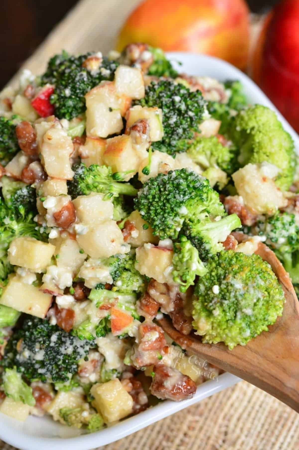 scooping gout some broccoli salad from the bowl filled with pear apple broccoli salad.