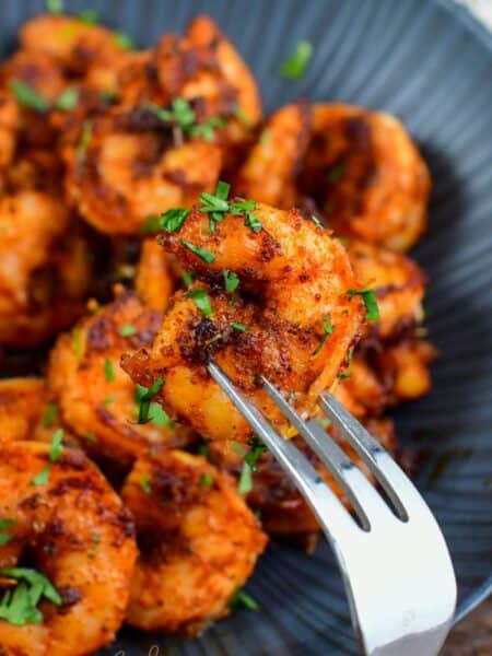 holding one blackened shrimp on a fork in front on a bowl.