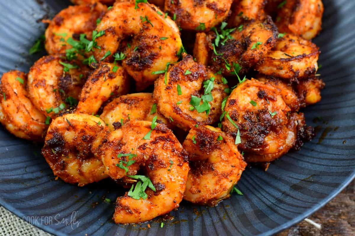 a pile of cooked blackened shrimp on a bowl topped with some parsley.