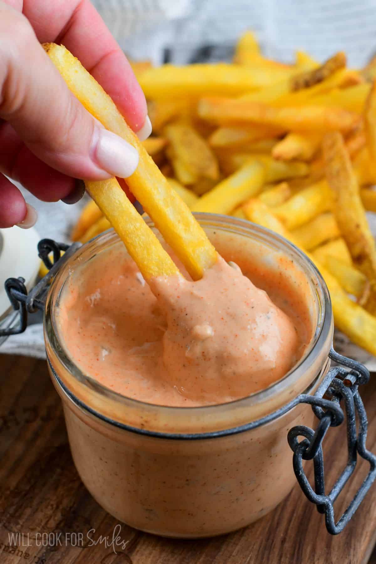dipping two fried into a jar of burger sauce.