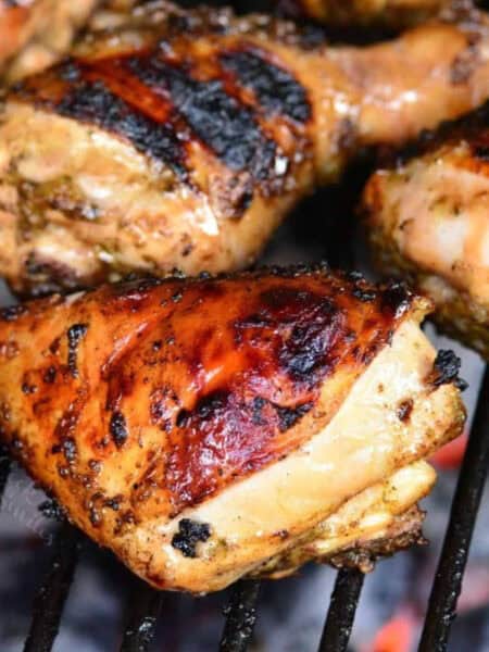 three jerk marinated chicken legs cooking on the charcoal grill.