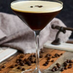 expresso martini in a glass on a wood surface with expresso beans as garnish.