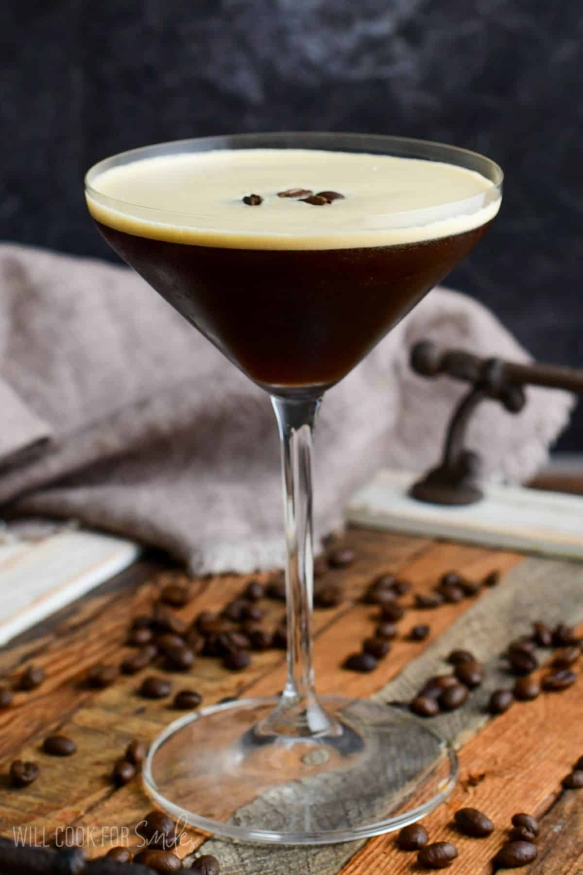 expresso martini in a glass on a wood surface with expresso beans as garnish.