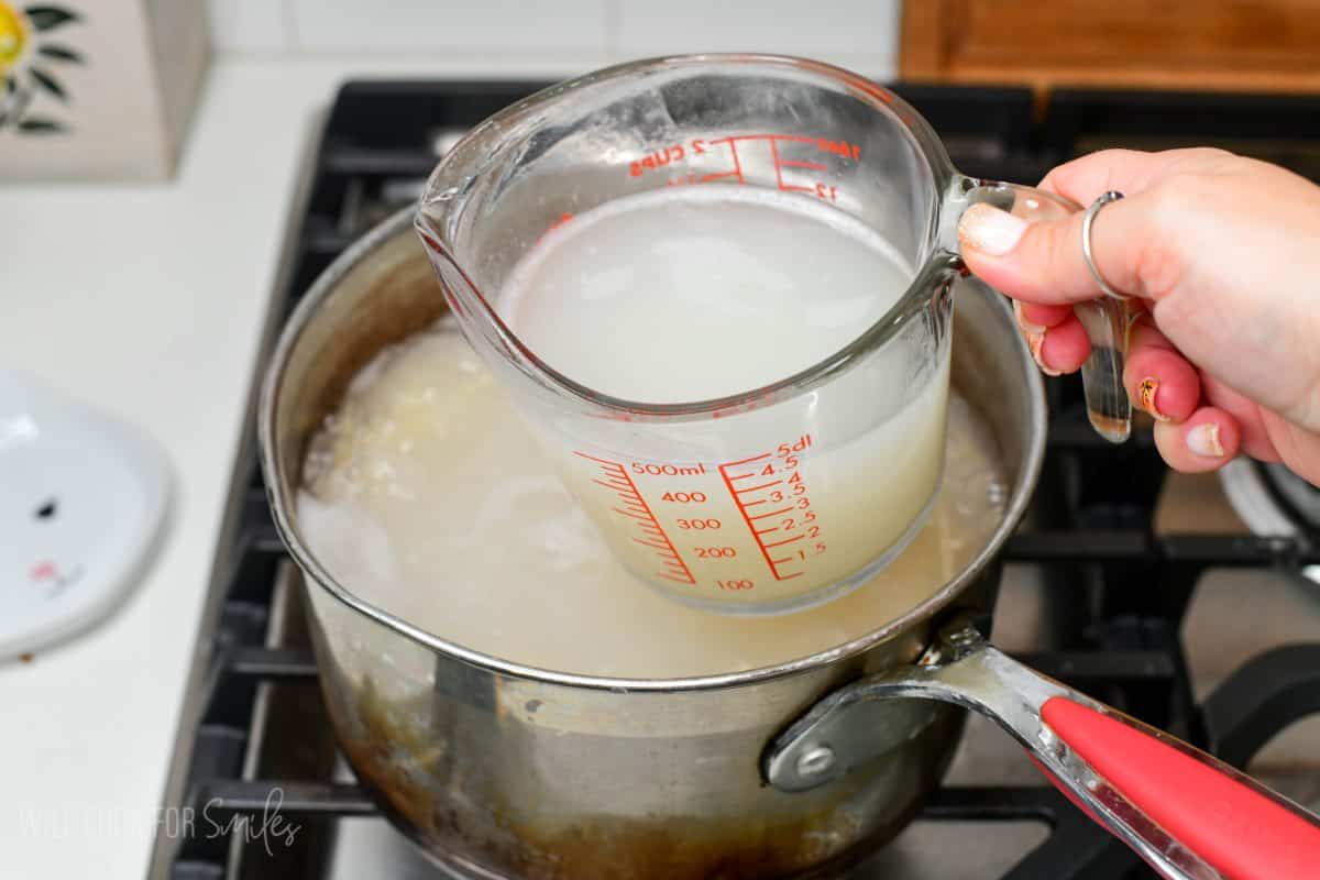 Scooping pasta water out of a pot with a measuring cup.