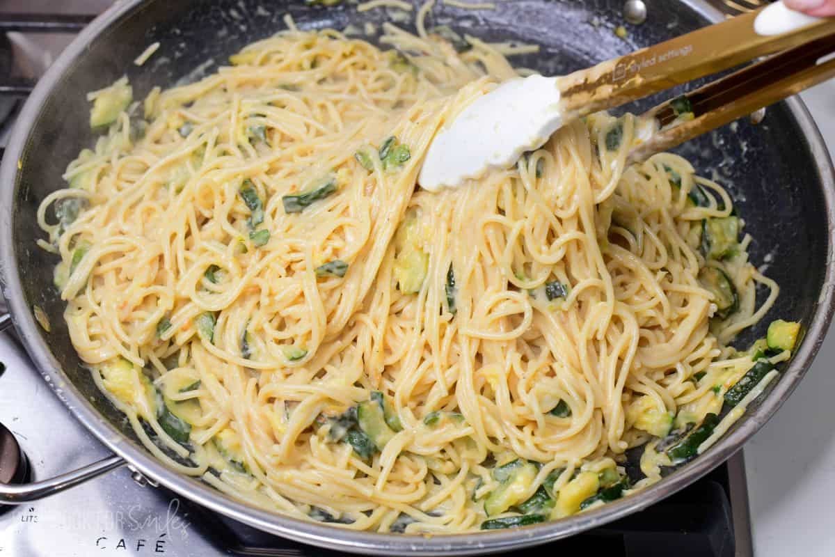 Stirring zuchini pasta in a pan on the stove with tongs.