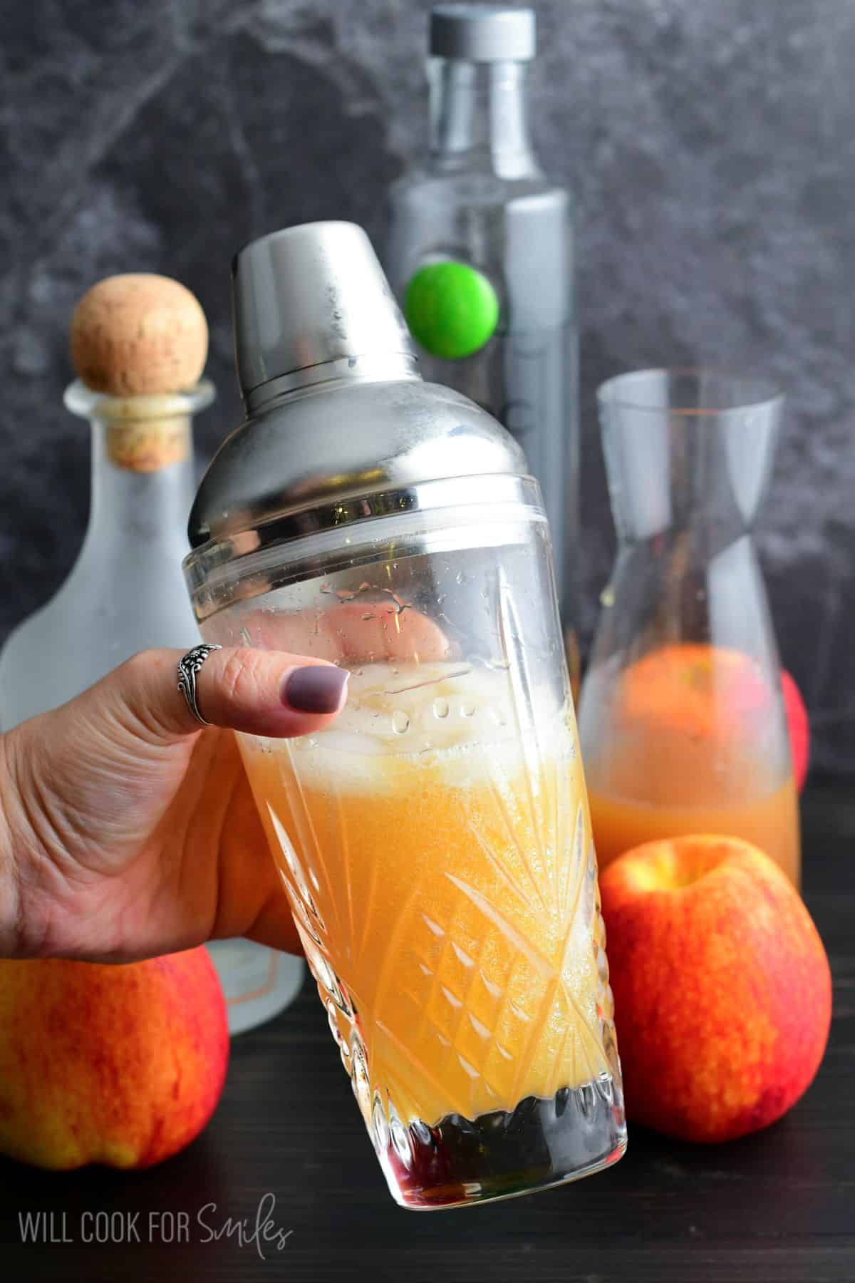 Shaking apple cider martin in a cocktail shaker with the ingredients in the background.