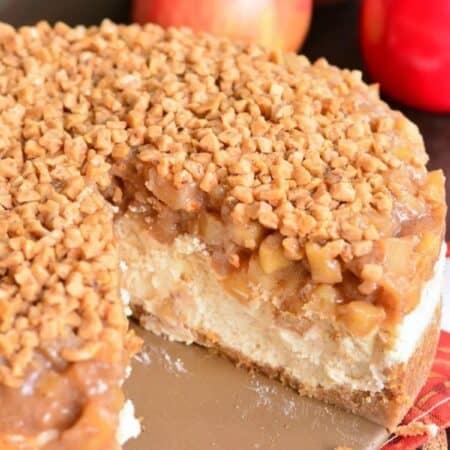 a whole apple cheesecake with a slice taken out next to apples.