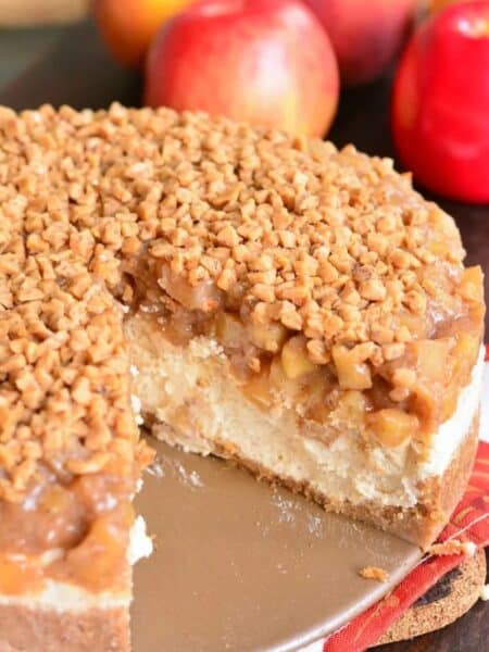 a whole apple cheesecake with a slice taken out next to apples.