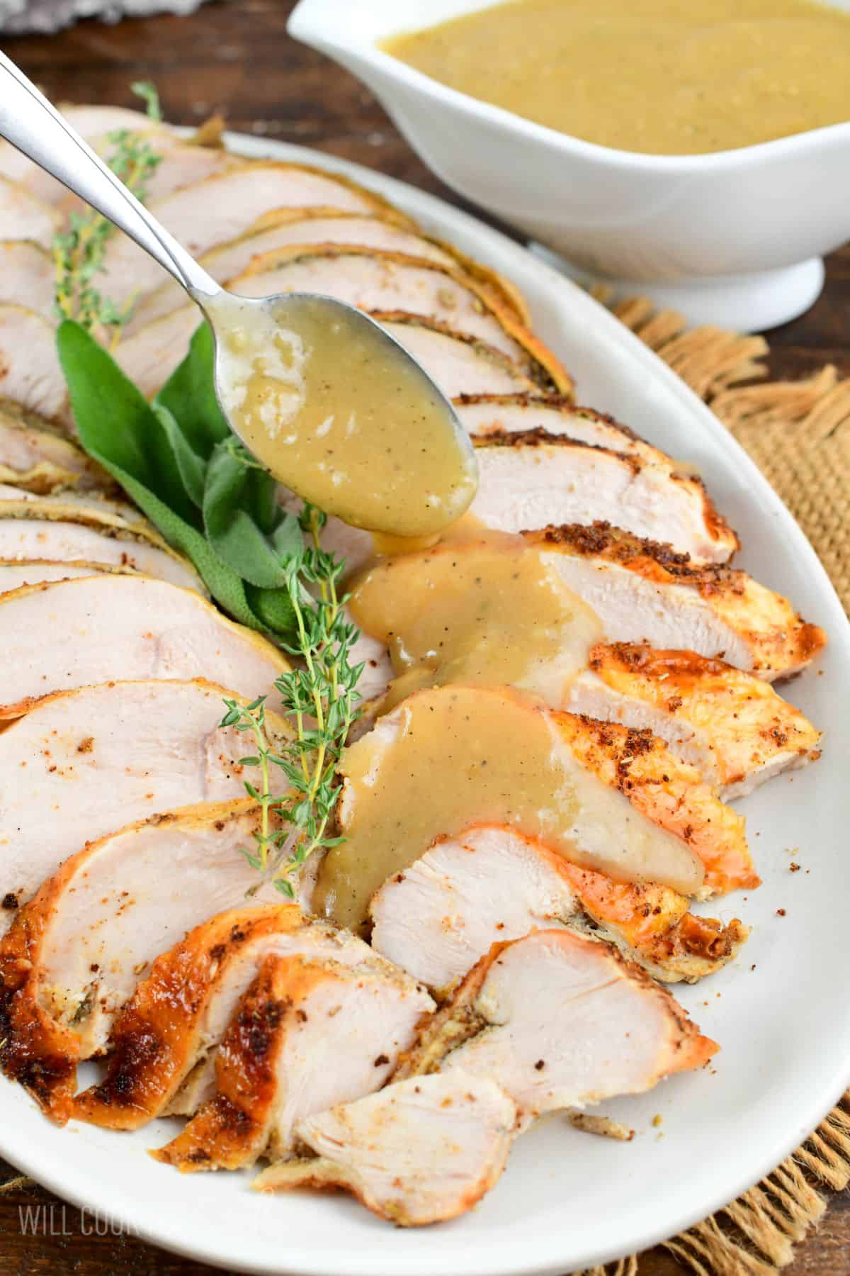 Pouring gravy from a spoon over sliced turkey breast on a plater.