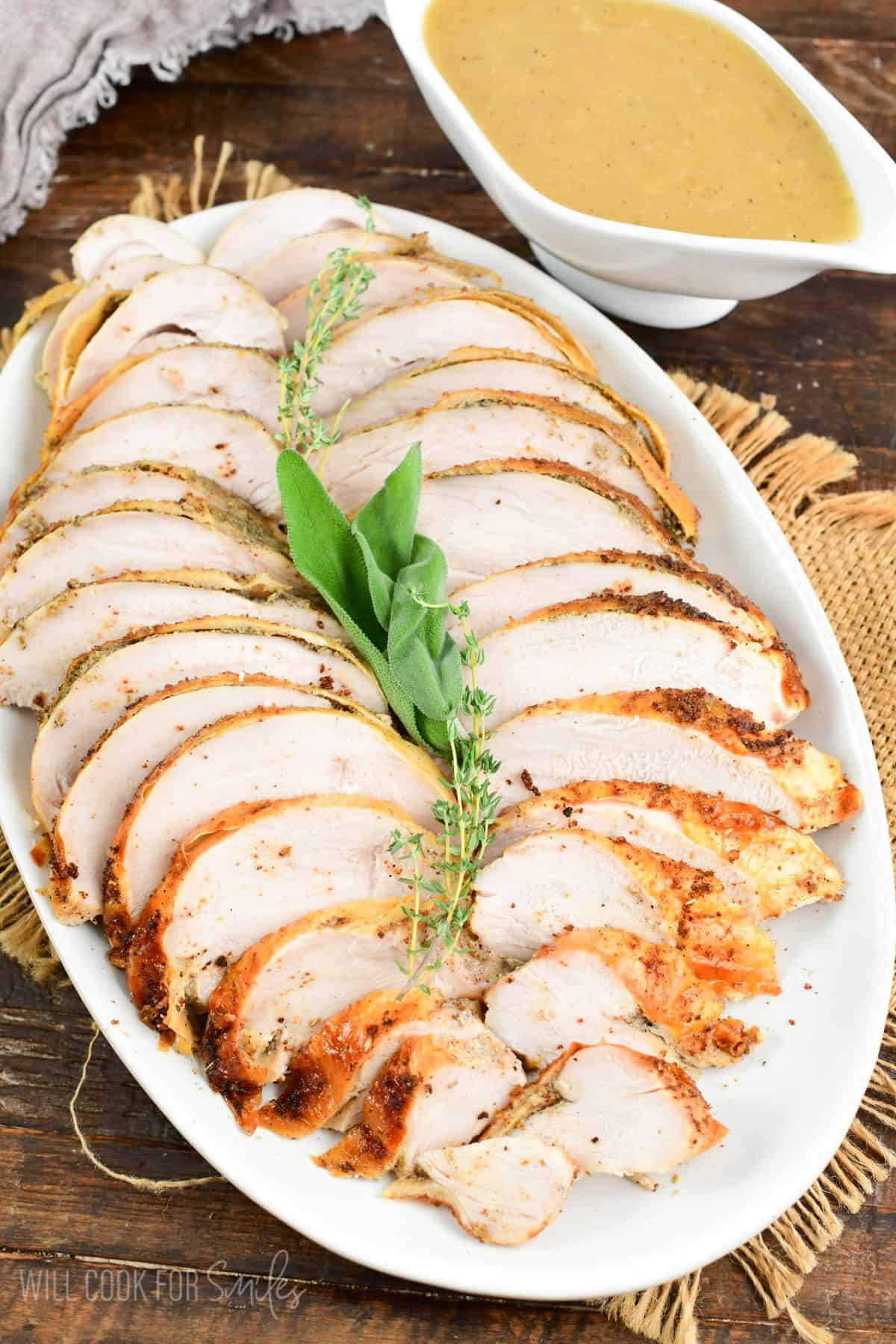 Sliced moist and tender roasted turkey breast on a platter with easy pan dripping gravy boat to the side.