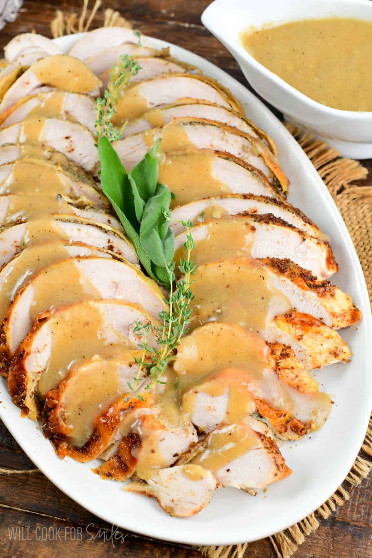 sliced herb roasted turkey breast on a plater with gravy on top.