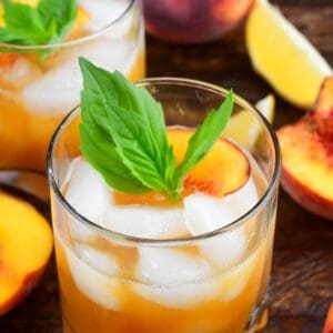 Peach smash bourbon in a glass with ice and peaches and mint on top as garnish.