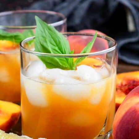 Peach bourbon smash in a glas with mint and peaches on top as garnish.