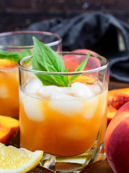 Peach bourbon smash in a glas with mint and peaches on top as garnish.