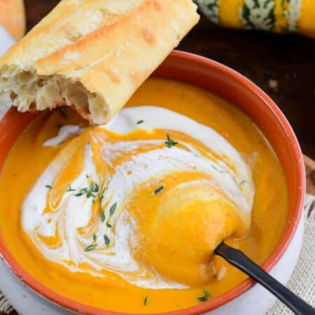 starting to spoon out some pumpkin soup drizzled with cream.