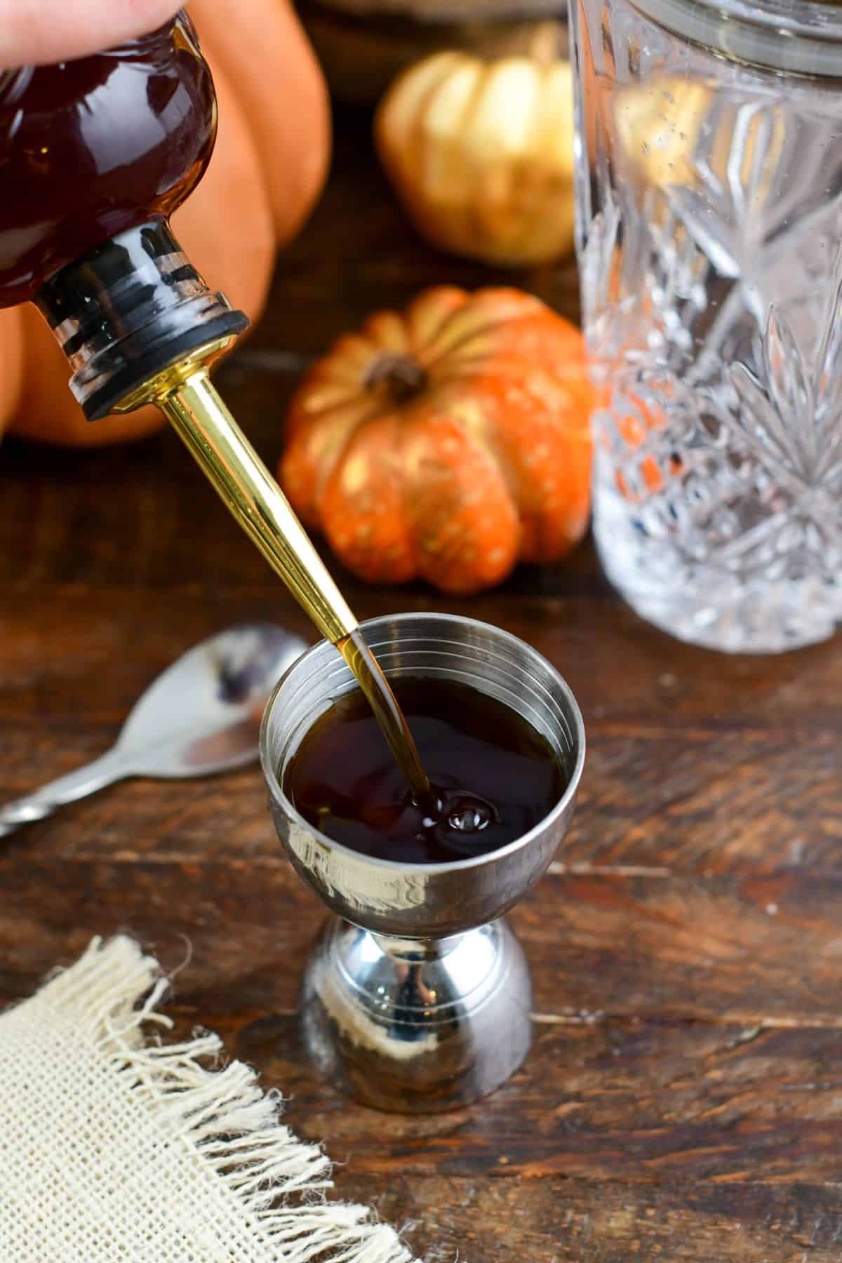 pouring pumpkin spice syrup into a jigger on a wood table.