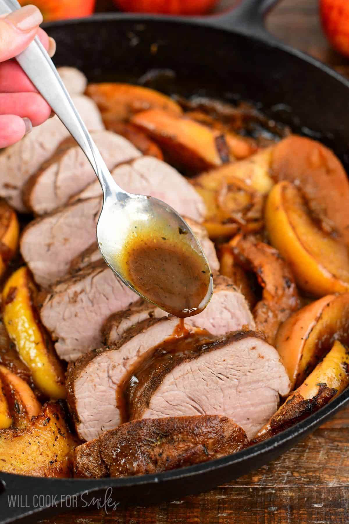 Pouring suace over roasted pork that is in a cast iron skillet with apples.