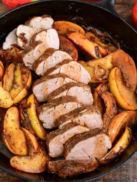 sliced roasted pork with apples in a cast iron skillet.