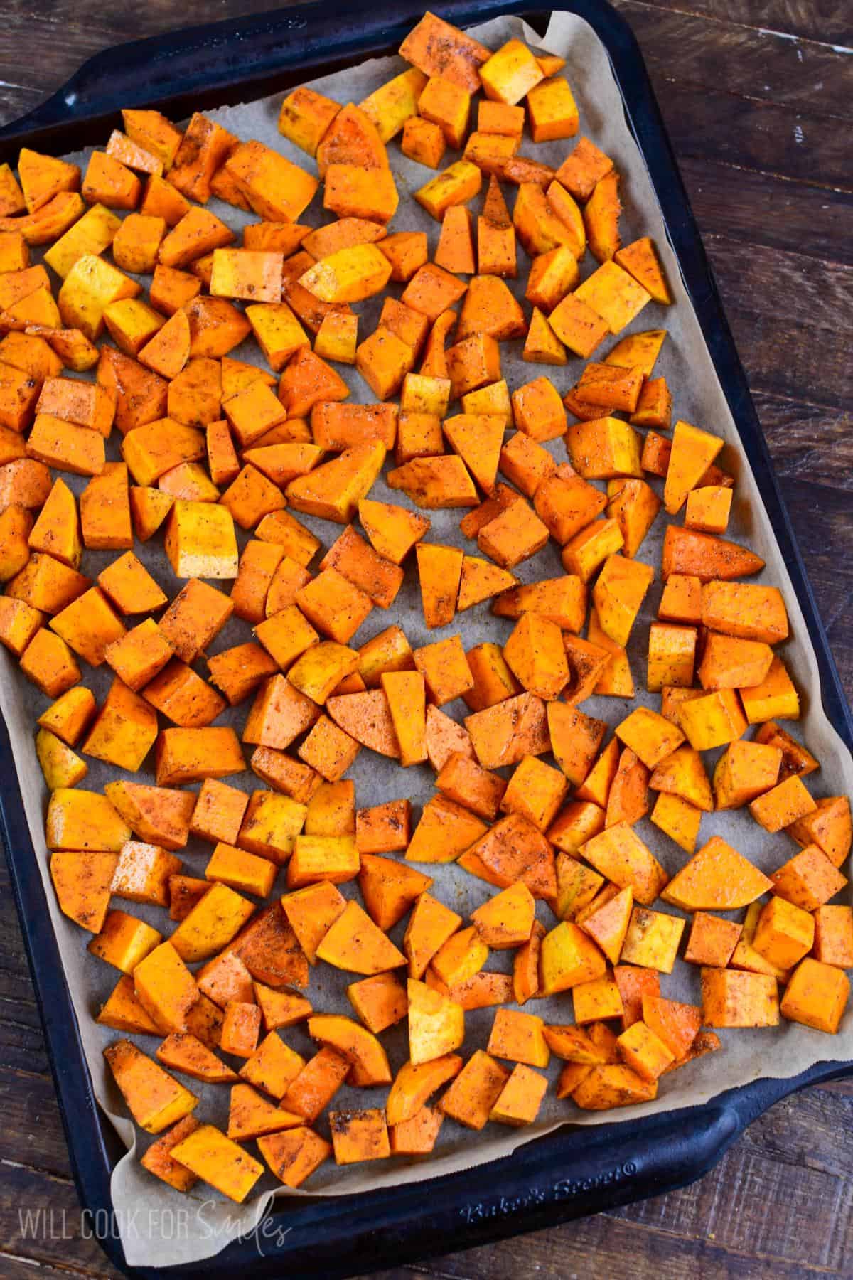 Honeynut squash spread on a parechment paper lined baking sheet on a wood surface.