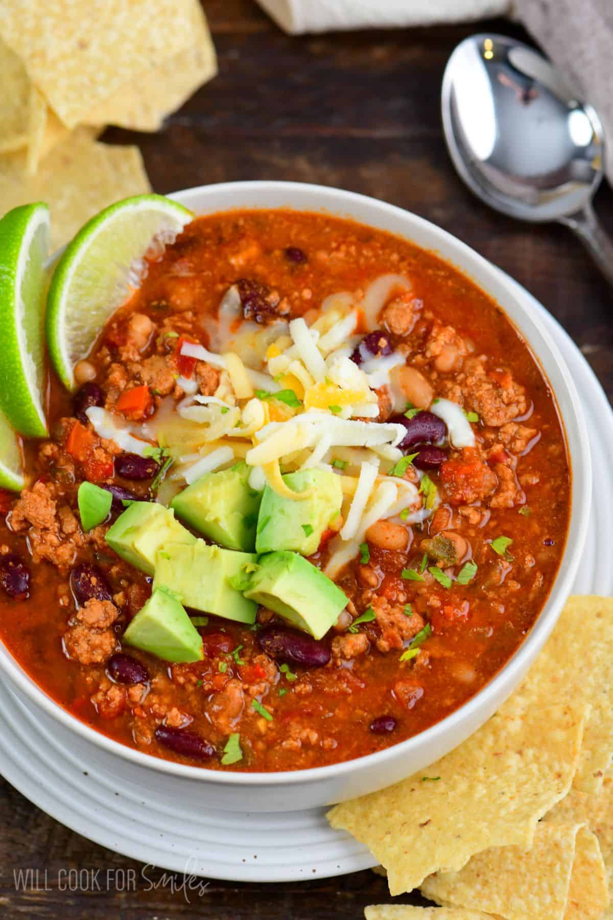 turkey chili in a bowl topped with lime slices, avocado, and shredded cheese.