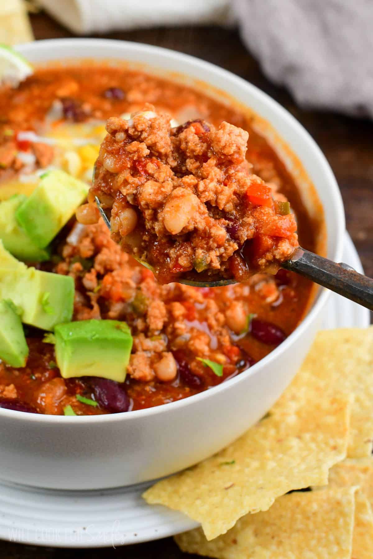 some turkey chili scooped on a soup spoon holding it over the bowl.
