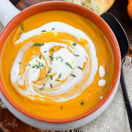 rustic bowl of smooth pumpkin soup with a swirl of cream and some thyme on top.