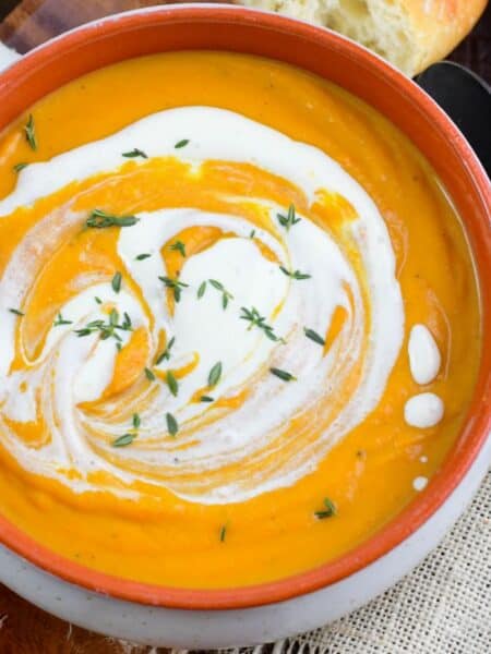 rustic bowl of smooth pumpkin soup with a swirl of cream and some thyme on top.
