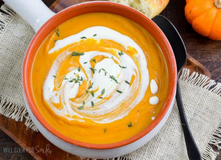 rustic bowl of smooth pumpkin soup with a swirl of cream and some thyme on top.