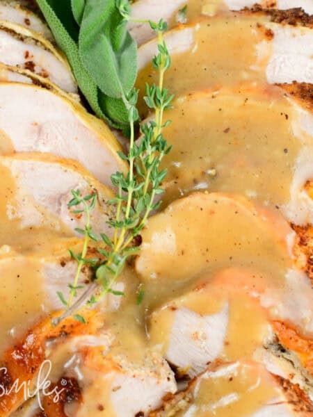 Sliced roasted turkey breast topped with golden gravy and herbs, served on a holiday white platter for Thanksgiving dinner.