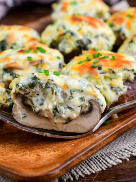 half of a creamy spinach artichoke stuffed mushroom on a fork next to others.