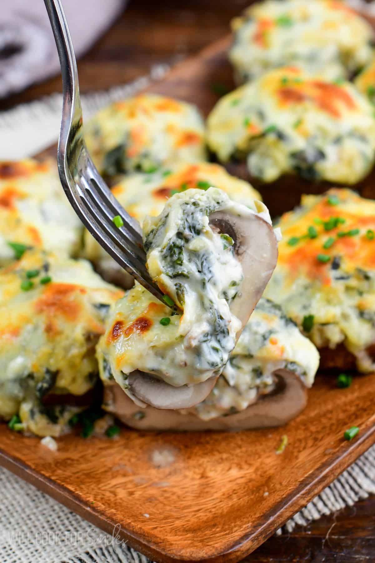 holding sliced mushroom stuffed with creamy spinach artichoke mixture and melted cheese on top.