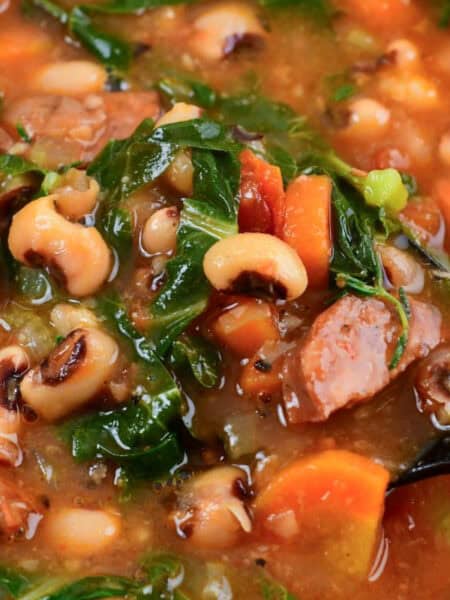 Bowl of hearty black eyed pea soup with andouille sausage, collard greens, and tomatoes in a rich broth.