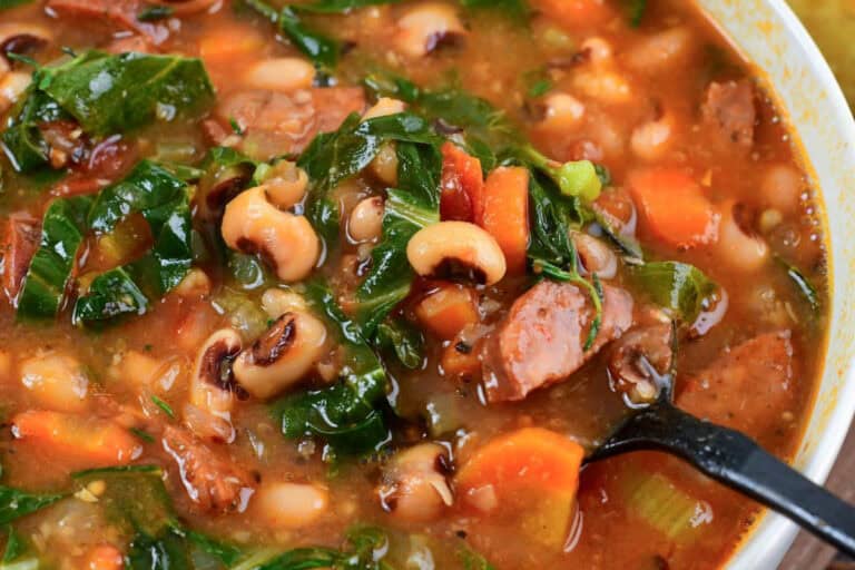 Bowl of hearty black eyed pea soup with andouille sausage, collard greens, and tomatoes in a rich broth.