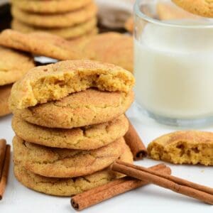 several soft and chewy snickerdoodle cookies stacked and some split in half next to glass of milk.