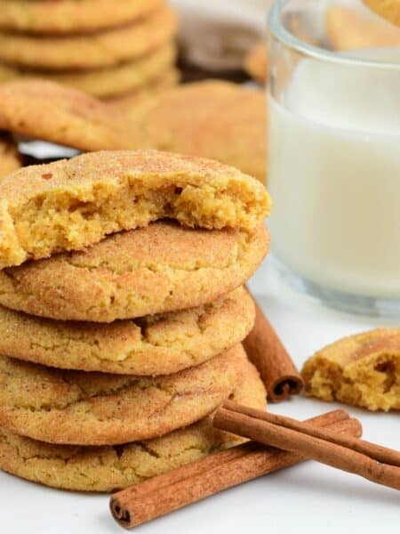 several soft and chewy snickerdoodle cookies stacked and some split in half next to glass of milk.