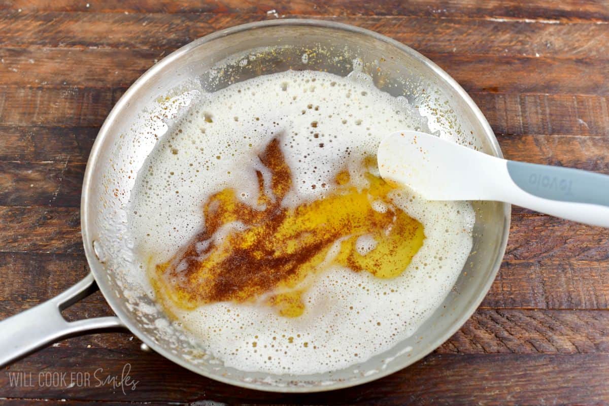 Amber colored brown butter in a stainless steel cooking pan with a spatula.