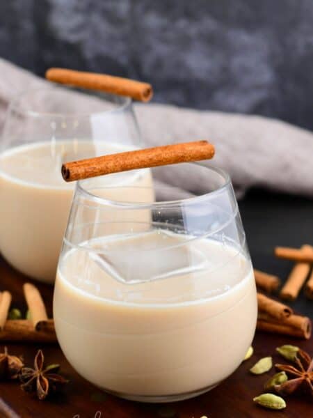creamy chai cocktail in a glass with an ice cube and cinnamon stick.
