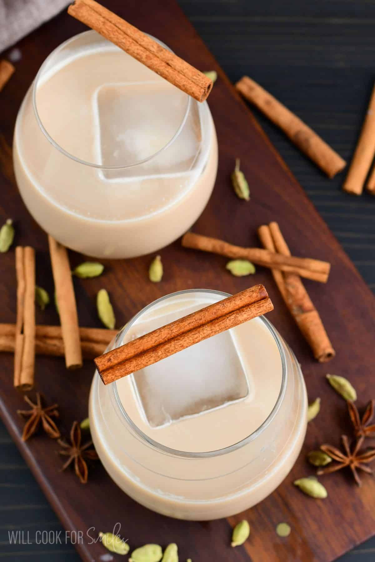 creamy chai cocktail in a glass with an ice cube and cinnamon stick across both of the glasses.