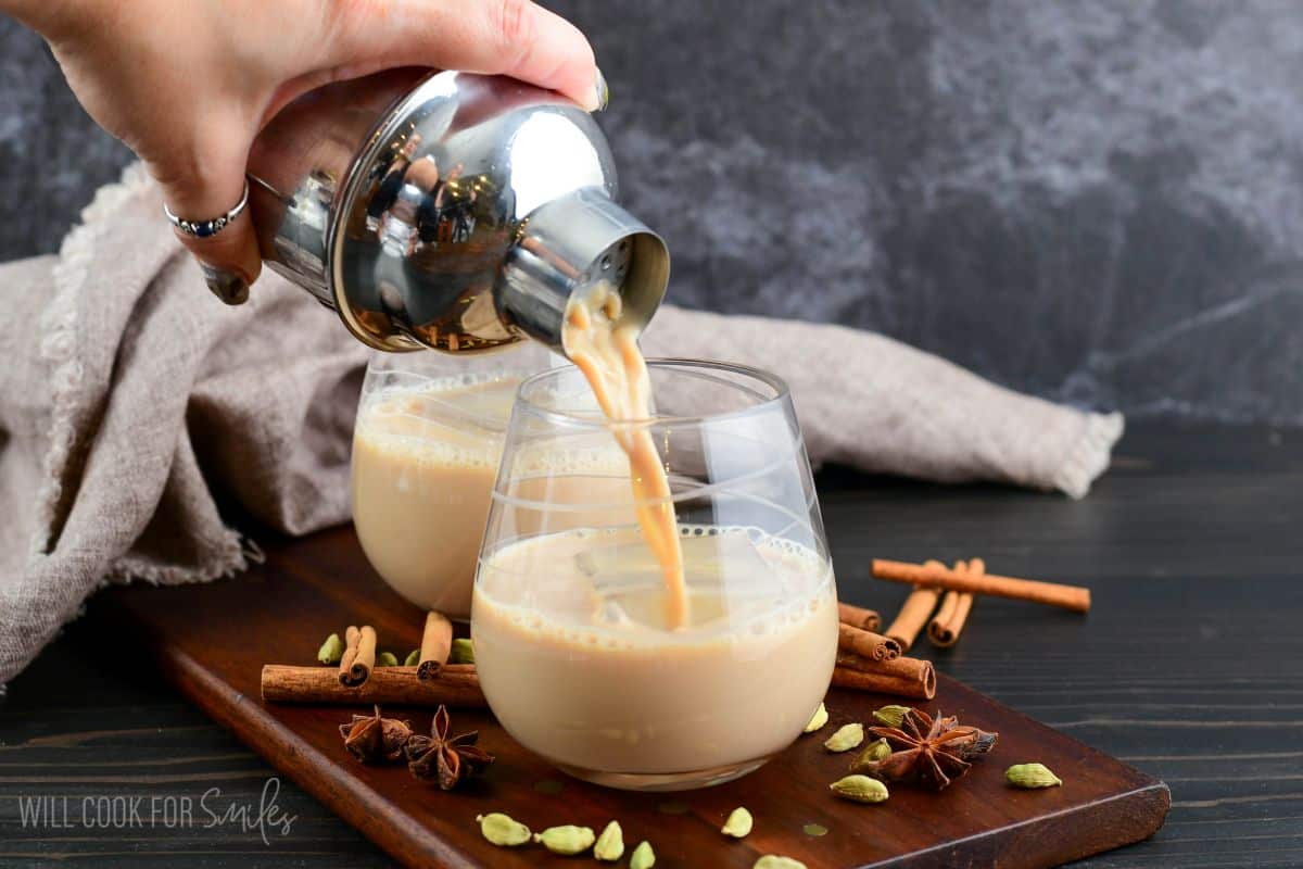 Pouring the creamy Chai cocktail from the cocktail shaker into a glass with an ice cube.