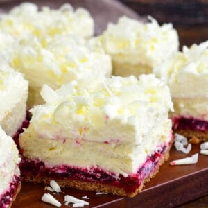 Cut Christmas cheesecake bars with white chocolate shavings on a wood surface.