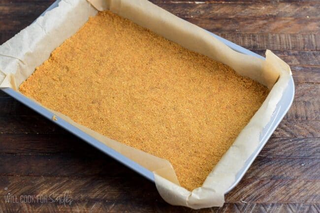 Crust for Christmas Cheesecake in a dish lined with parchment paper on a wood surface.