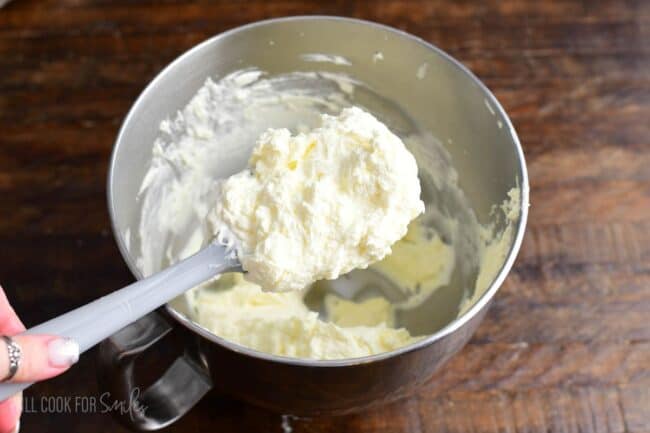 mixed light and smooth white chocolate mousse frosting on the spatula over a bowl.