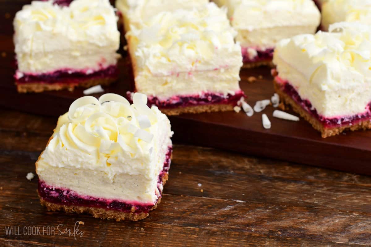 One slice of Christmas Cheesecake Bars (White Chocolate Cranberry Cheesecake Bars) next to the board with others on top of board.