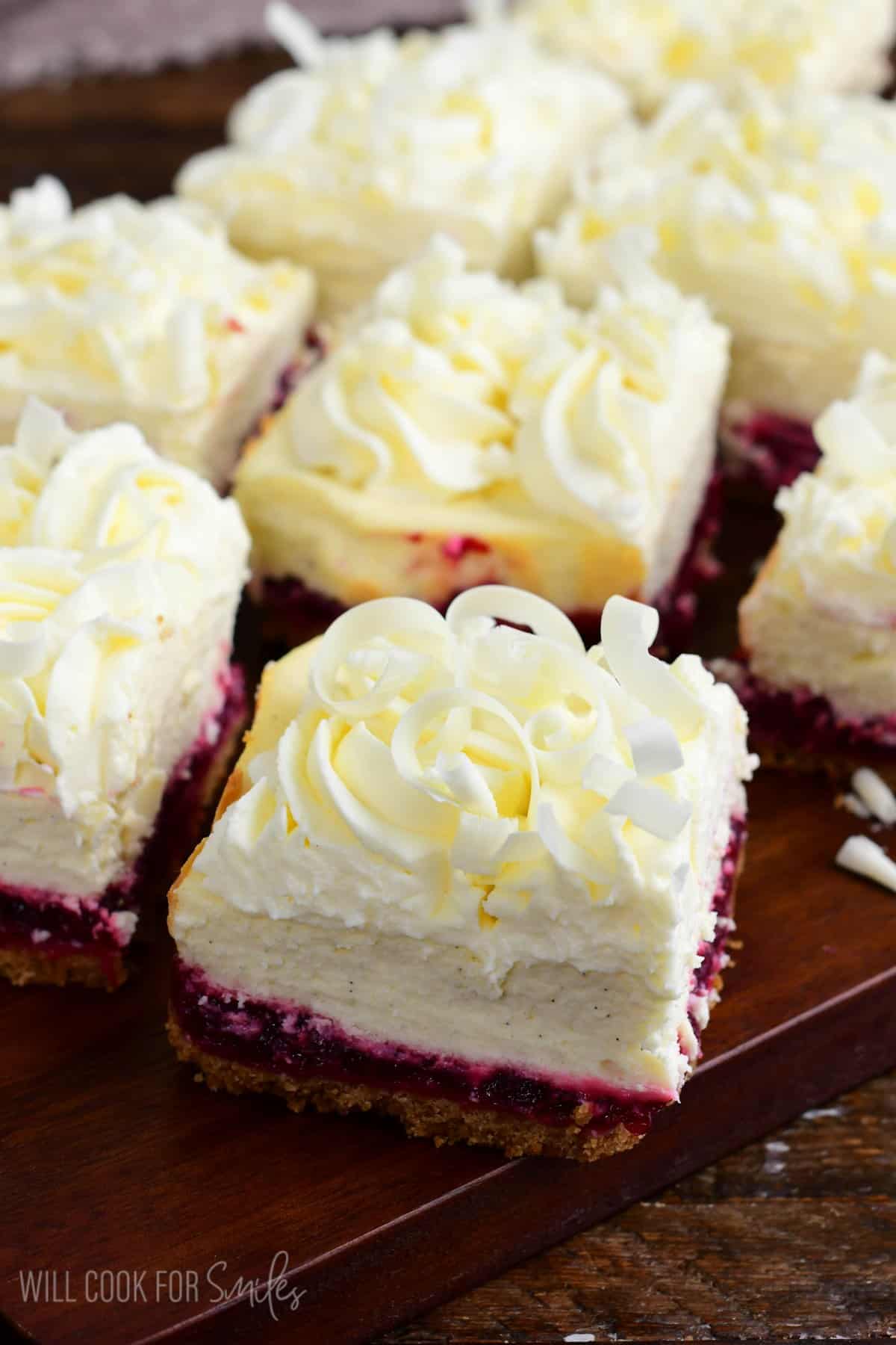 Christmas cheesecake bars with white chocolate shavings on a wood surface.